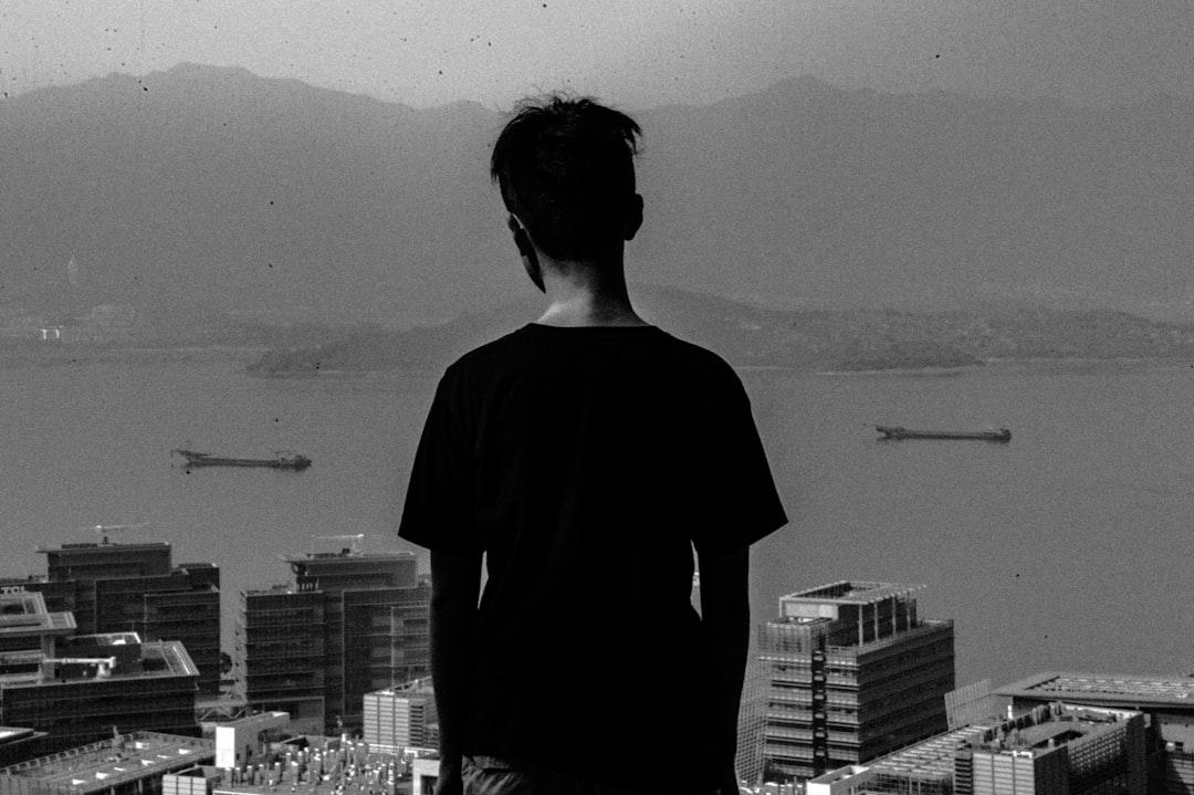 grayscale photo of man standing with city overview