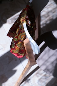 A colorful dashiki draped over a chair with a statue and a stack of books nearby, bathed in warm natural light.