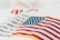 An embroidered American flag patch with vivid red and white stripes and blue stars on a white fabric background. Some out-of-focus text appears behind, adding depth to the image.