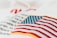 An embroidered American flag patch with vivid red and white stripes and blue stars on a white fabric background. Some out-of-focus text appears behind, adding depth to the image.