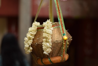 A woven basket decorated with a garland of white flowers hangs by colorful ribbons. It appears to be part of a traditional or cultural celebration, with intricate designs and embellishments.