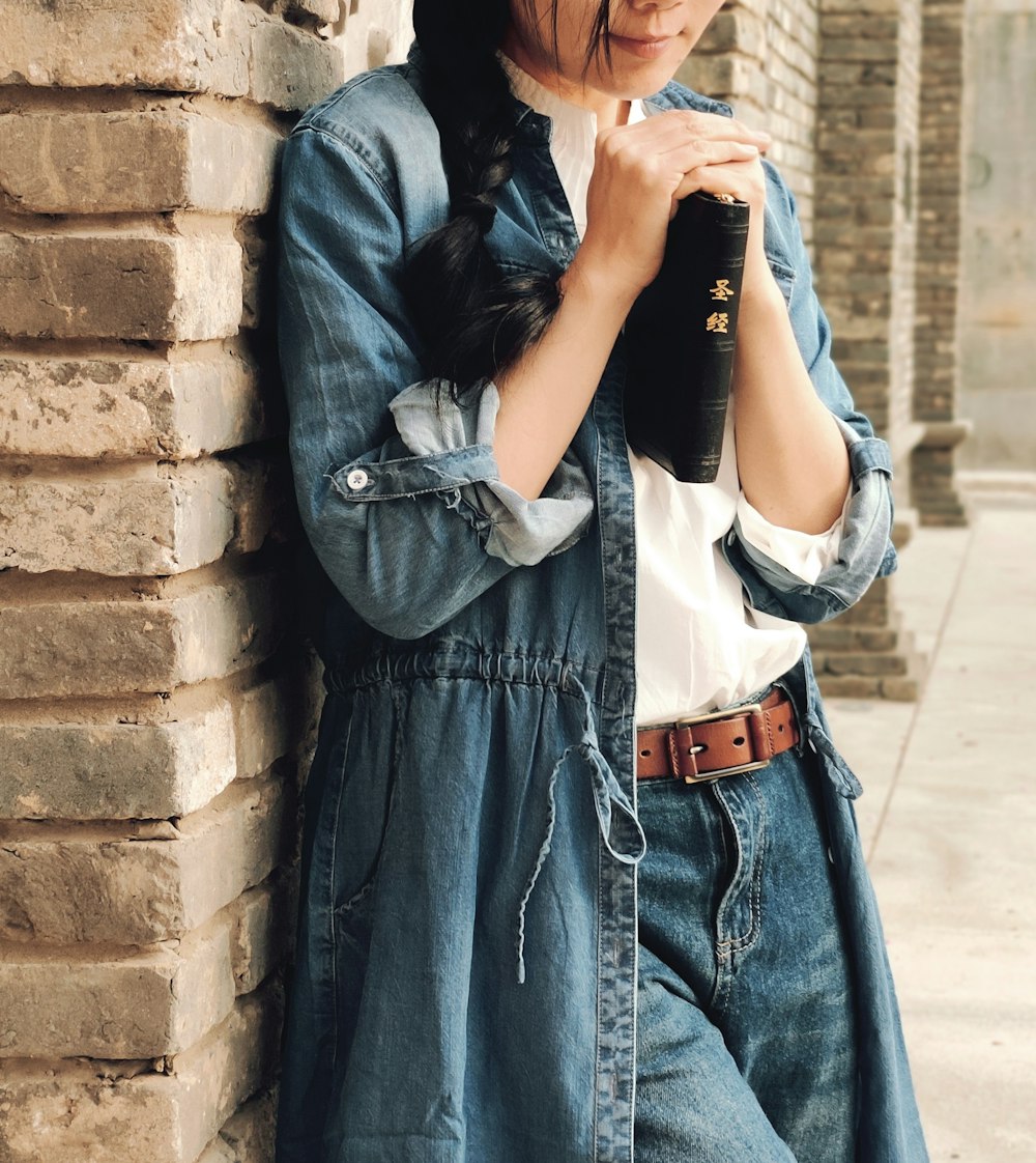 woman leaning beside brown wall while holding book