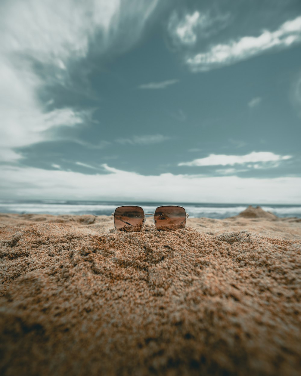 óculos de sol de lente marrom na areia na fotografia de baixo ângulo