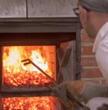 man picking with long rod on wood fired oven