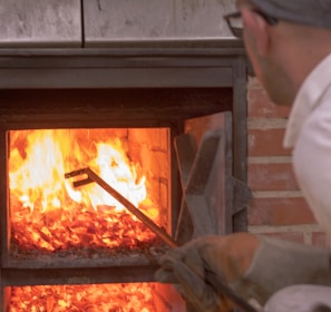 man picking with long rod on wood fired oven