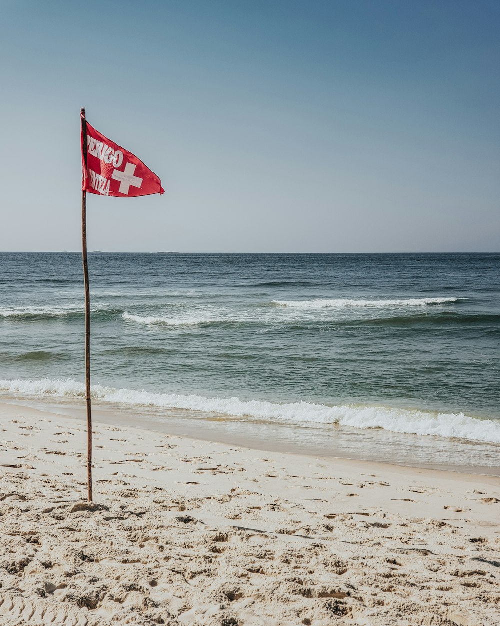 red flag near body of water under white sky