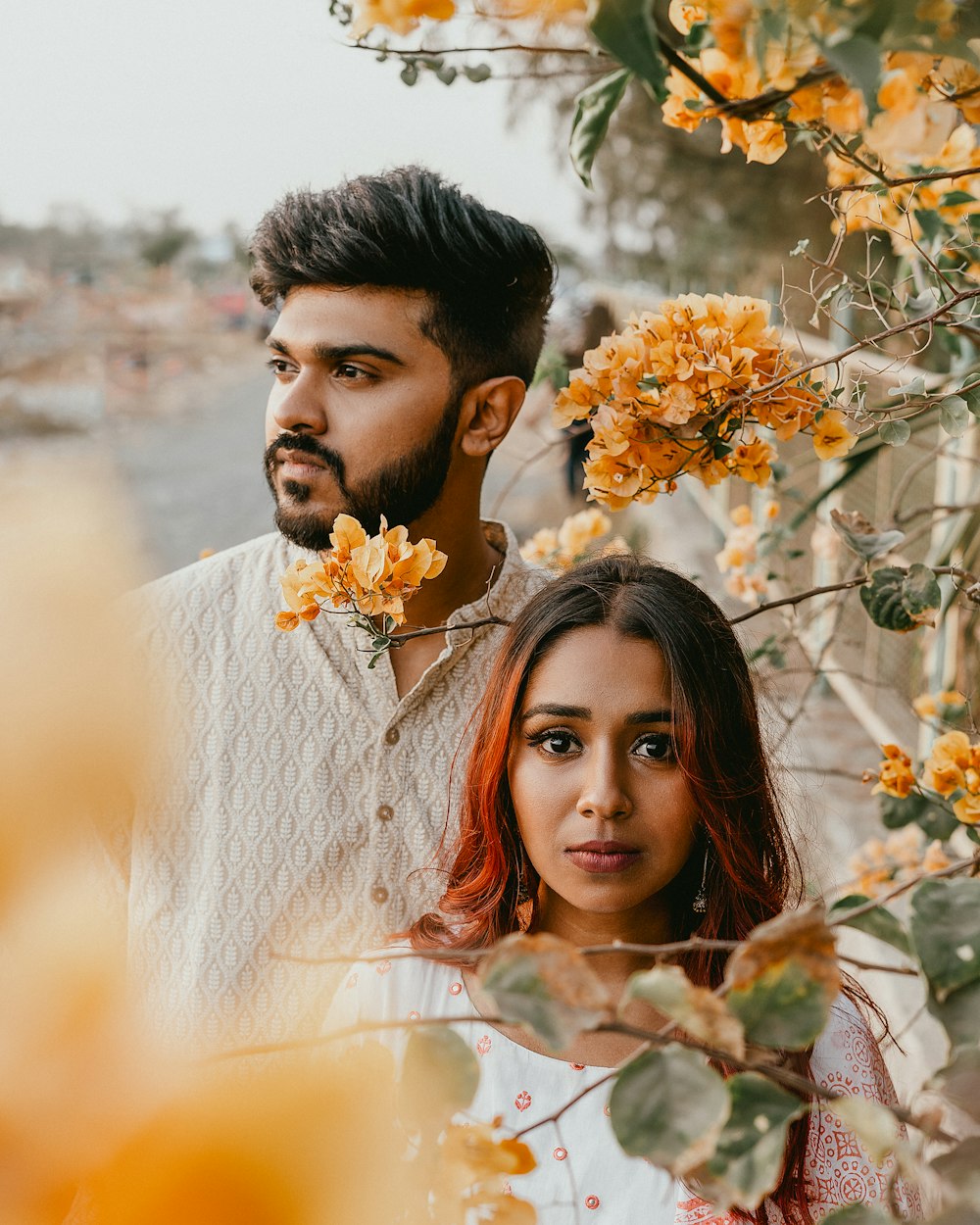 man standing behind woman wearing white top standing beside tree during daytime