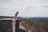 woman sitting on cliff's edge overlooking forest during daytime