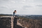 woman sitting on cliff's edge overlooking forest during daytime