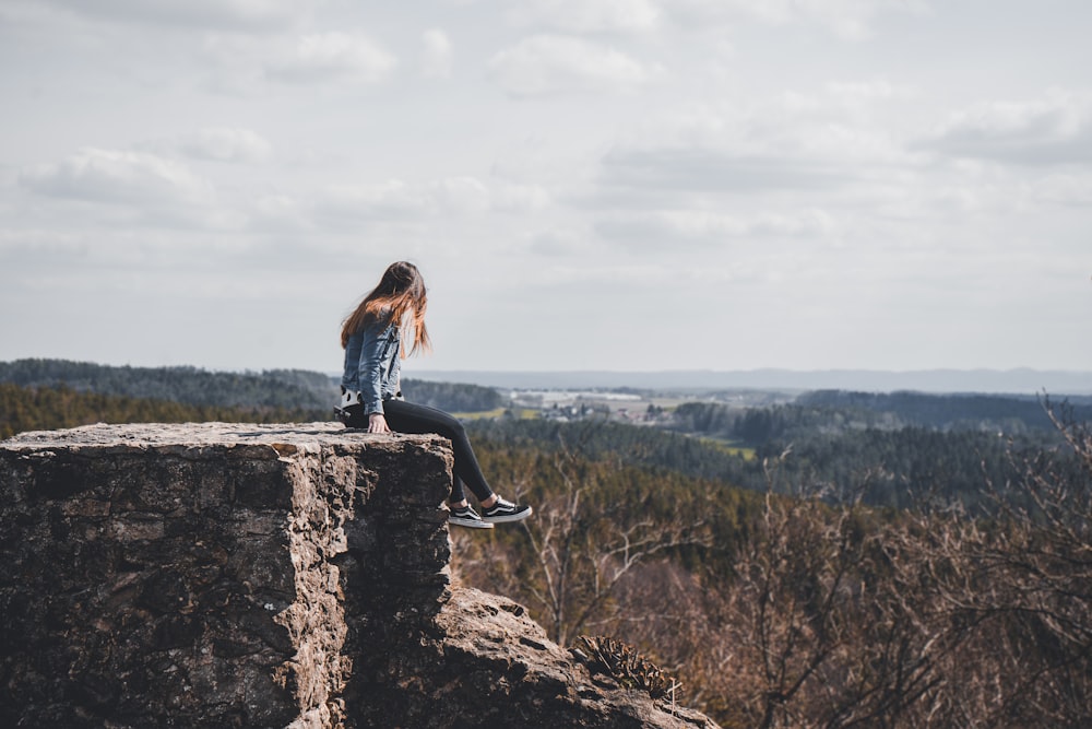 Femme assise sur le bord de la falaise surplombant la forêt pendant la journée