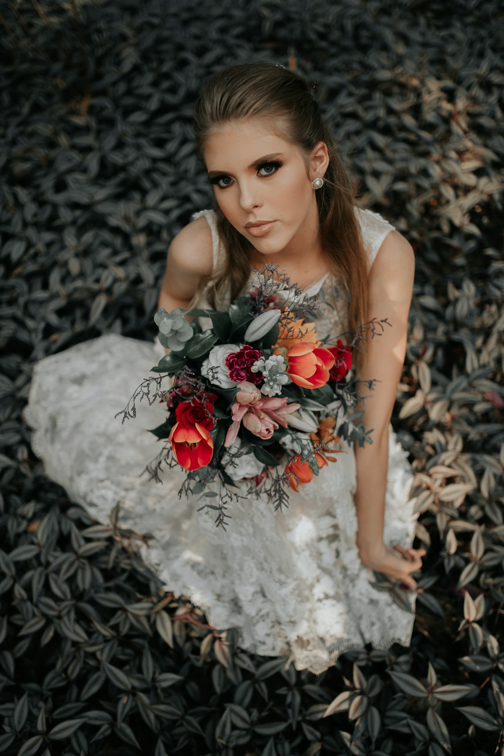 woman sitting on grass field while holding flower bouquet