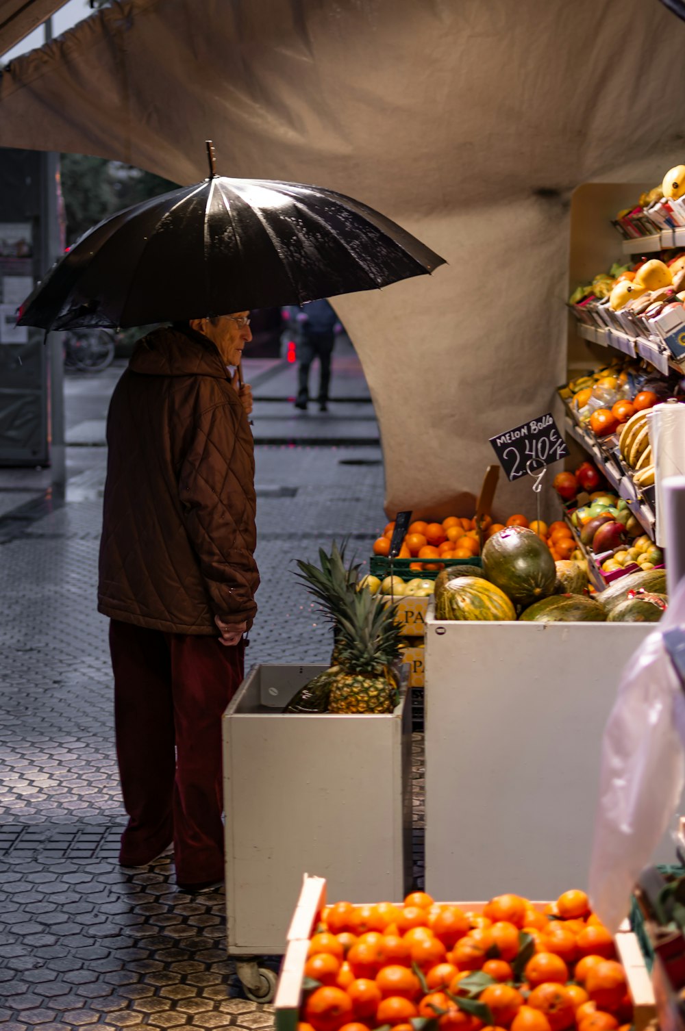 hombre de pie frente al puesto de frutas mientras sostiene un paraguas negro