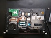 A laptop with its back cover removed, revealing various internal components including a cooling fan, circuit boards, copper heat pipes, and RAM modules. The layout shows intricate electronic parts and connectors.