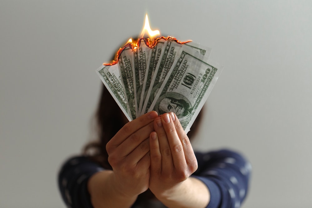 A woman holds a fan of burning banknotes