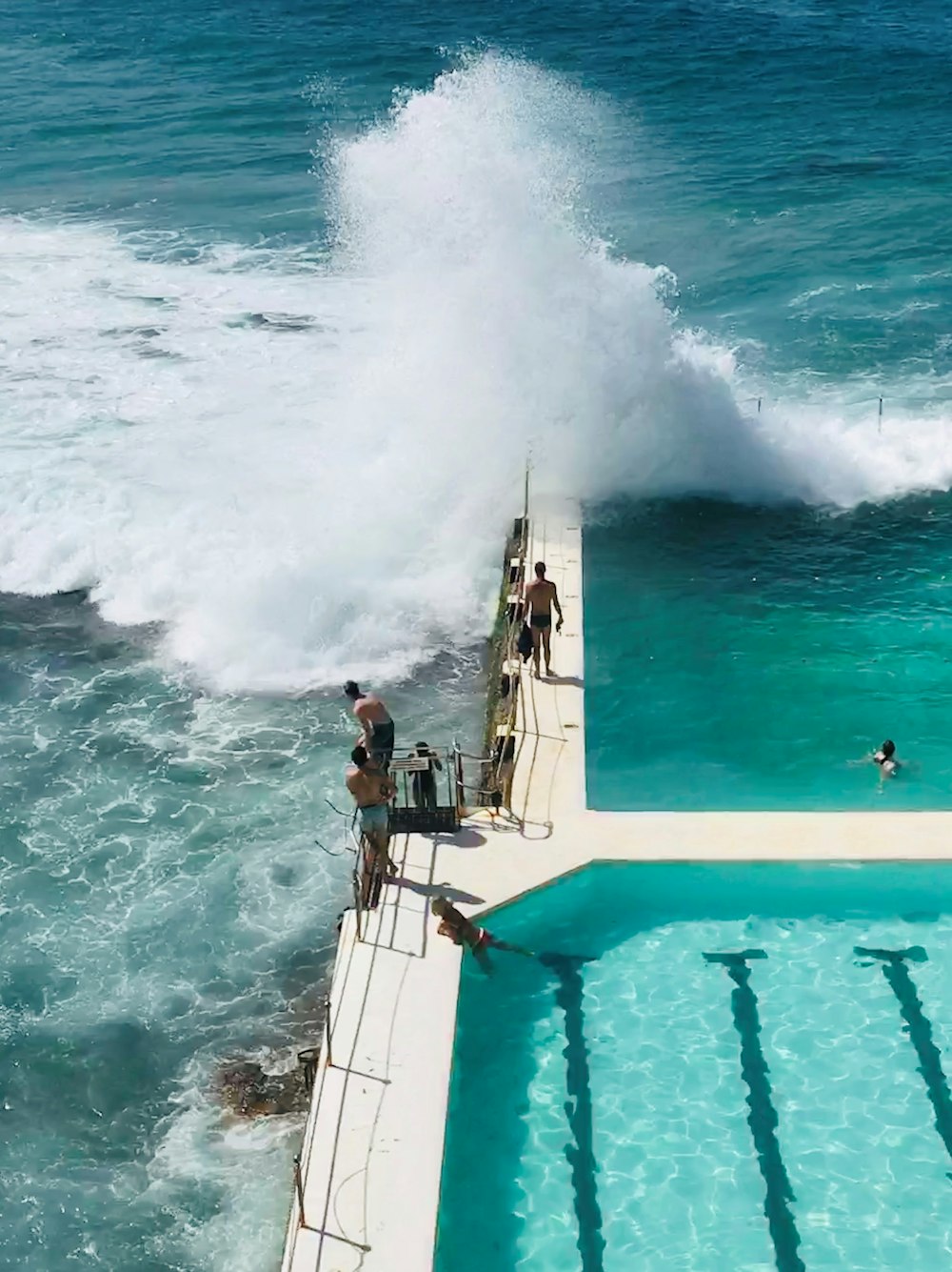 three men standing on pool edge while looking at the sea wave crashed
