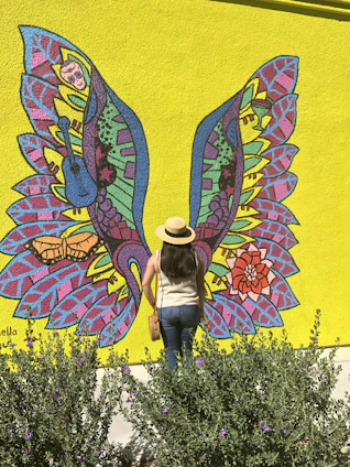 A vibrant urban mural featuring colorful monarch butterflies soaring above a group of diverse young people learning styling techniques.