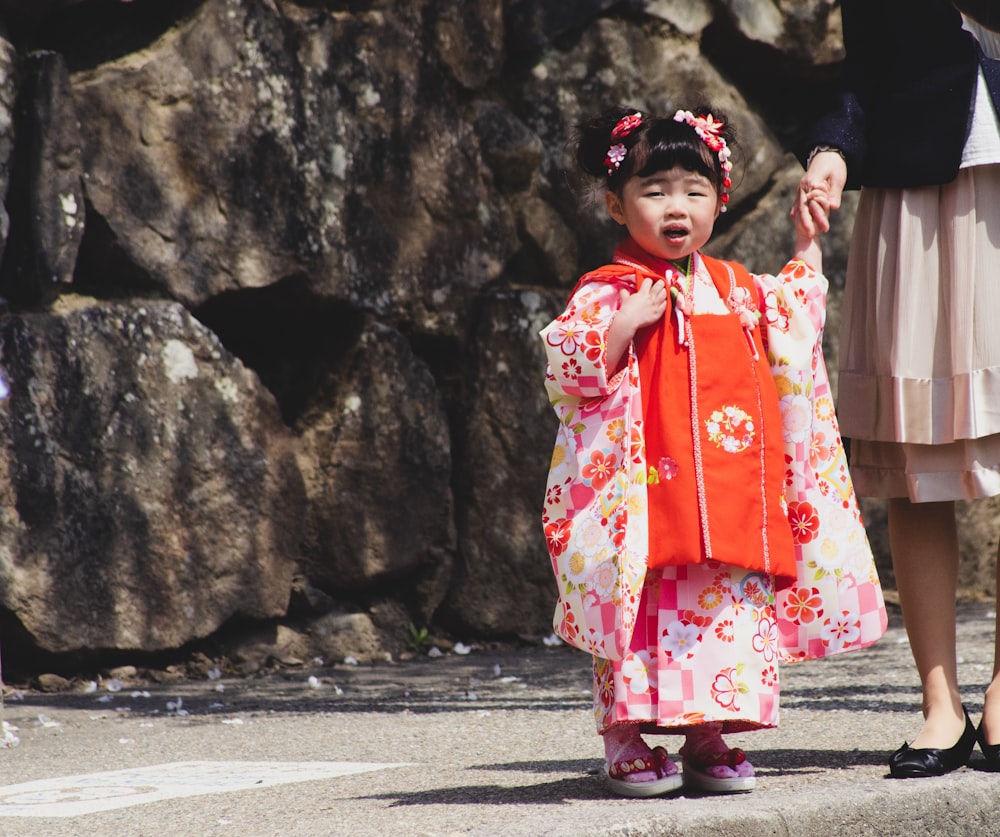 a little girl in a kimono standing next to a rock wall