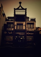 A building with a distinct architectural style features a shop on the ground floor called 'Turquoise Jewelry'. The facade has dark wooden elements and decorative balconies. The ambient lighting gives the image a dim, vintage look.