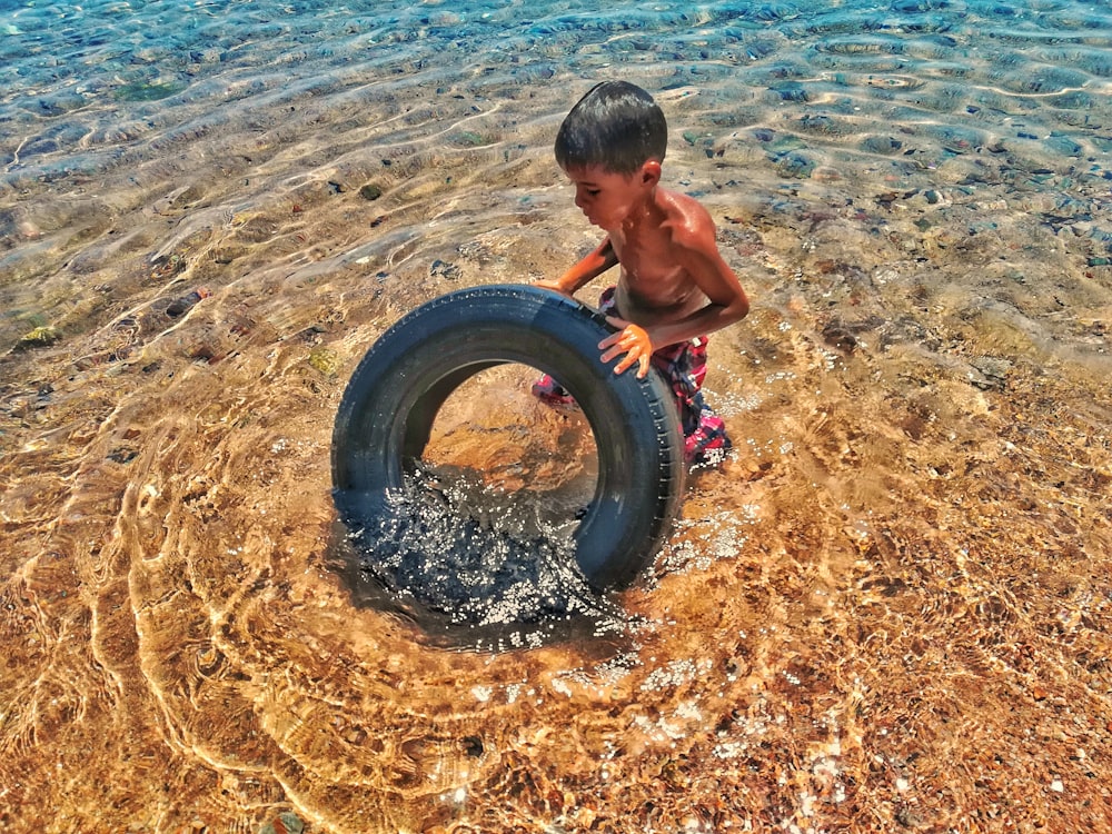 Un niño jugando con un neumático en el agua