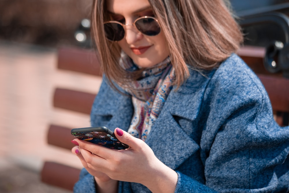 woman in blue coat using smartphone
