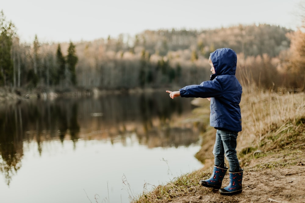 toddler wearing blue jacket pointing the river