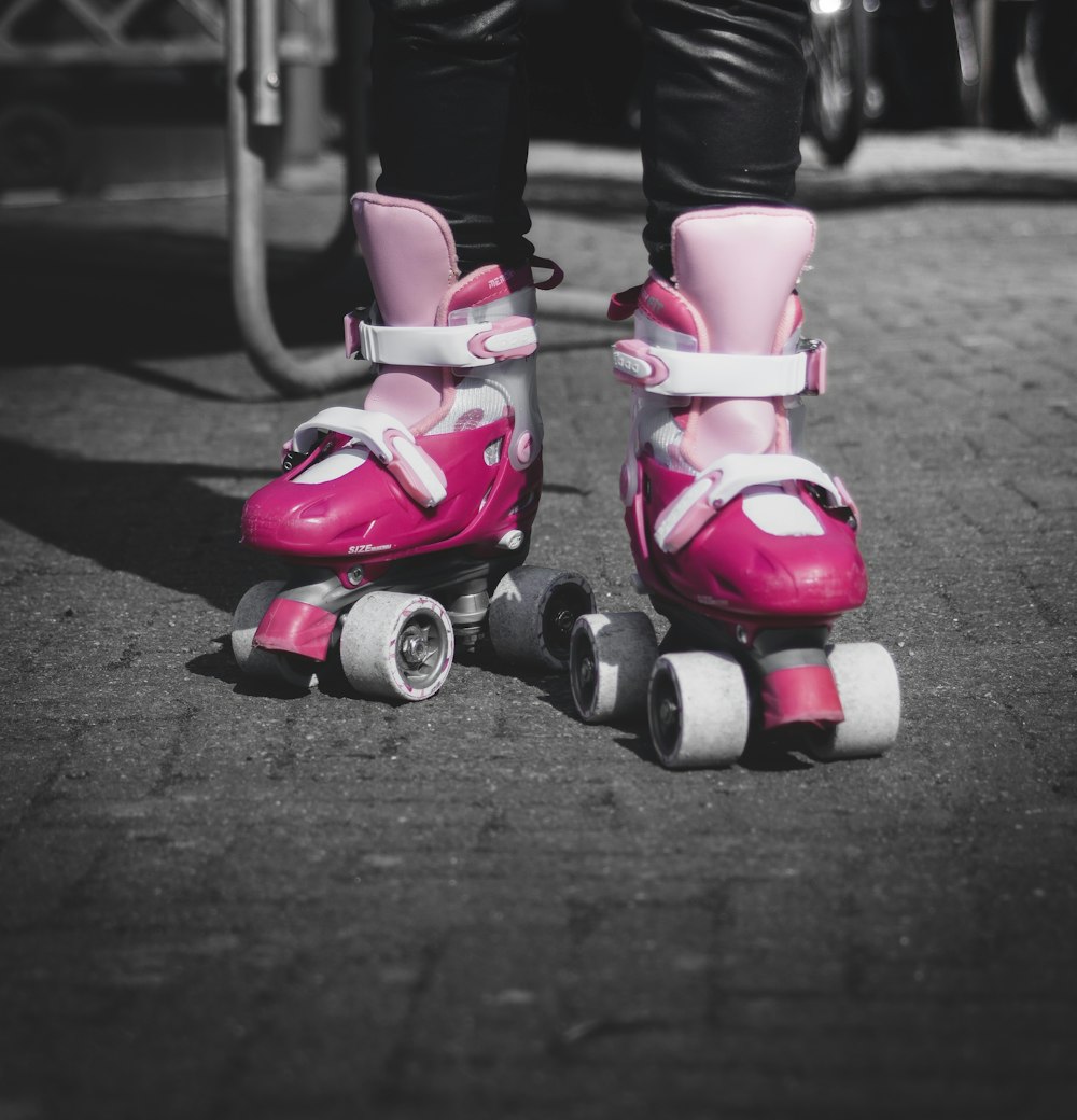 selective color photo of person wearing pair of pink roller skates