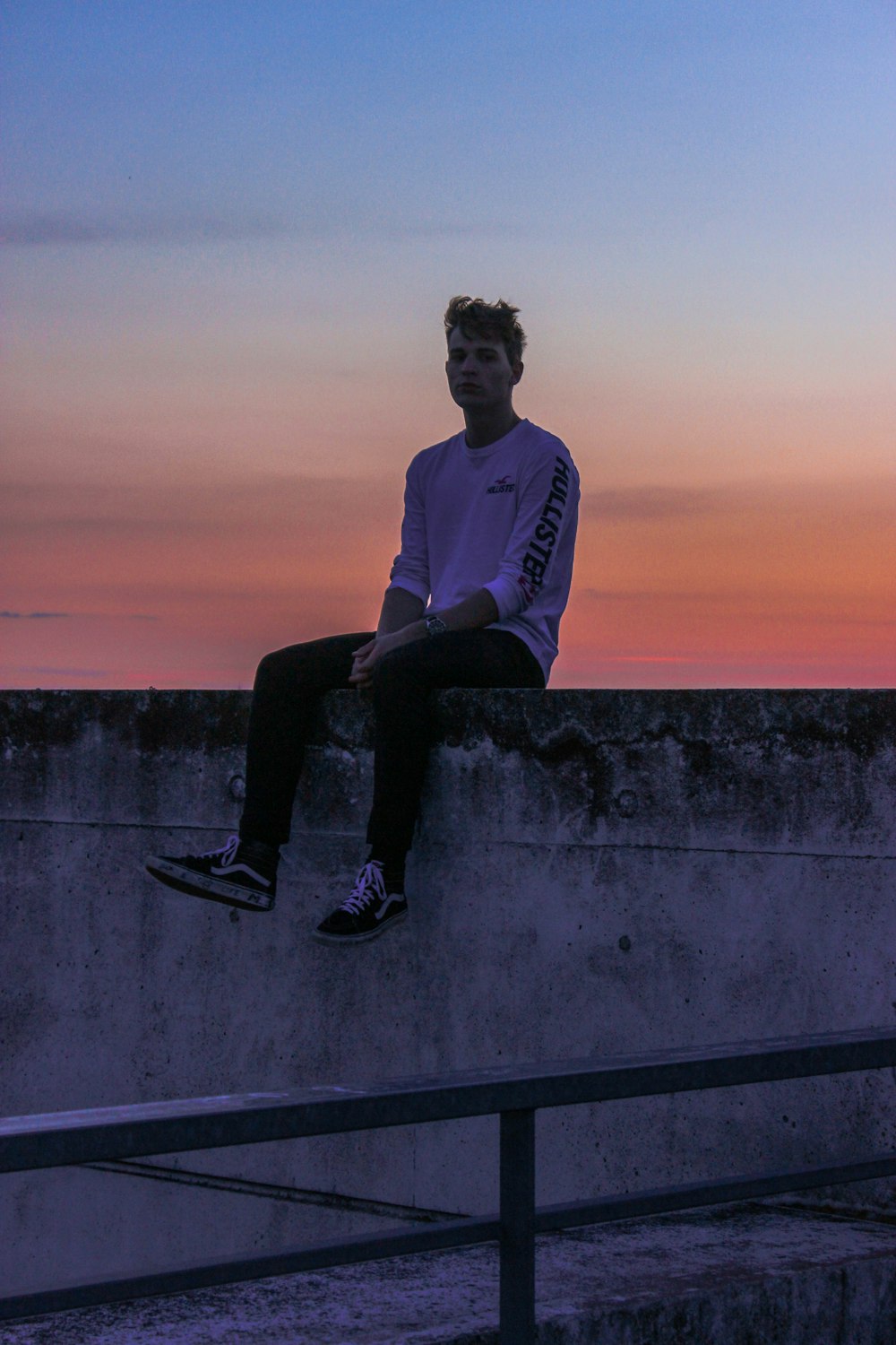 man wearing purple sweater sitting on wall