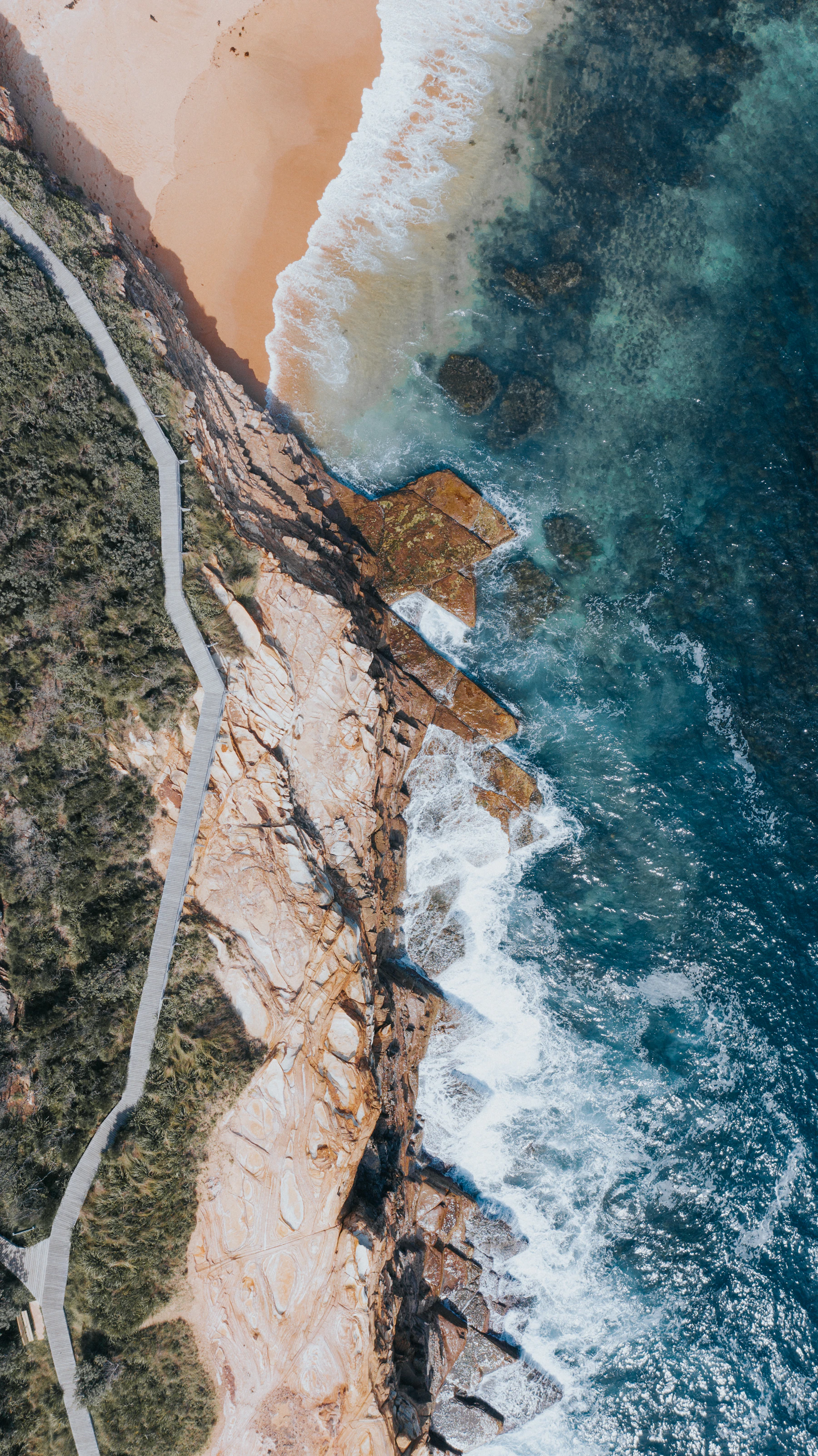 Dark ocean coastline from directly above, waves meeting the shore