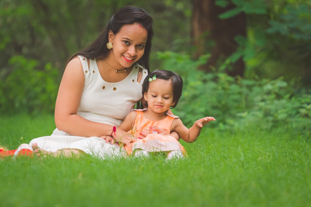 woman wearing white sleeveless dress sitting on grass field with toddler