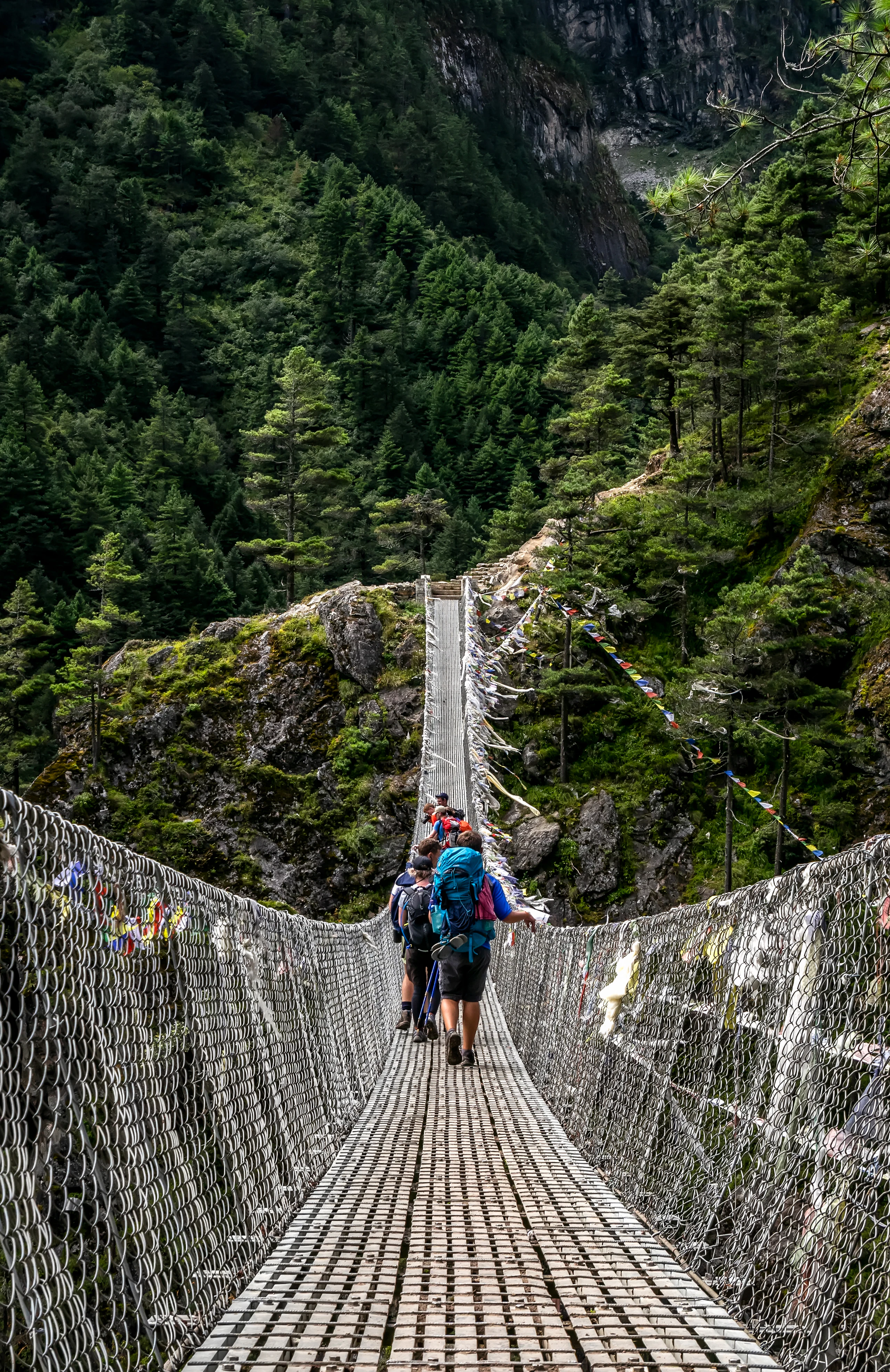 Trekkers crossing a high suspension bridge strung with prayer flags on a Himalayan trail, Nepal