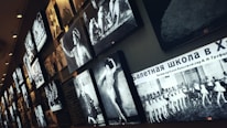 Several black and white photographs are displayed on a wall, featuring images of ballet dancers and scenes from performances. The arrangement appears to be part of an exhibition or gallery. There is text in Russian on one of the images.