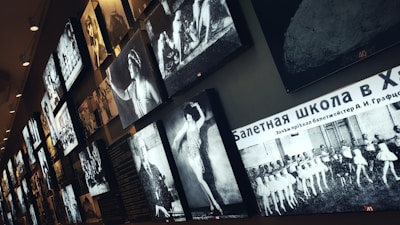 Several black and white photographs are displayed on a wall, featuring images of ballet dancers and scenes from performances. The arrangement appears to be part of an exhibition or gallery. There is text in Russian on one of the images.
