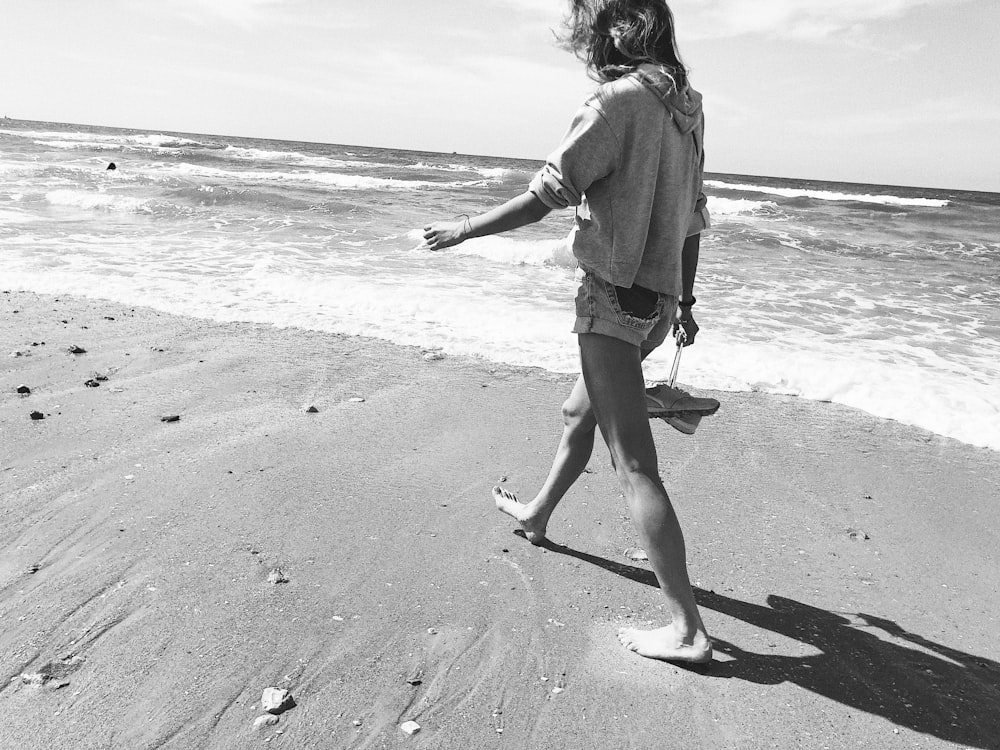 Mujer con sudadera con capucha y pantalones cortos caminando en la orilla del mar