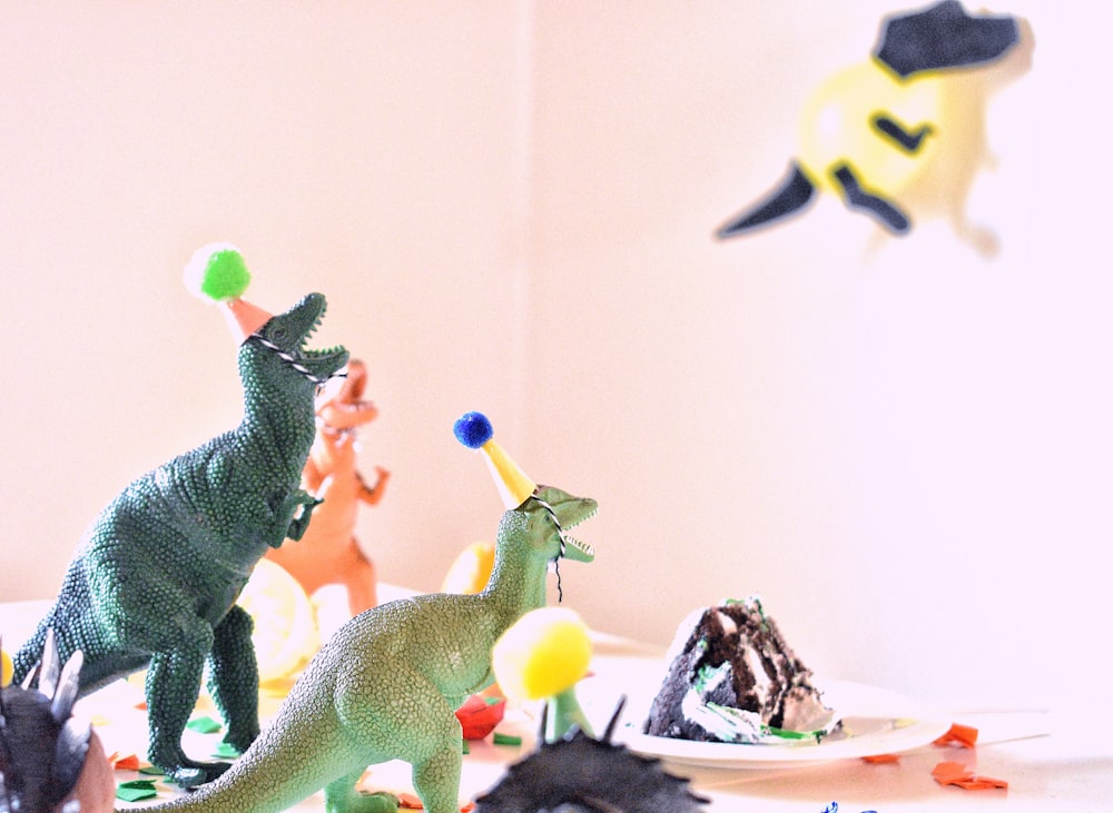 juguetes de dinosaurios de colores variados cerca de un pastel de rebanadas en una mesa blanca