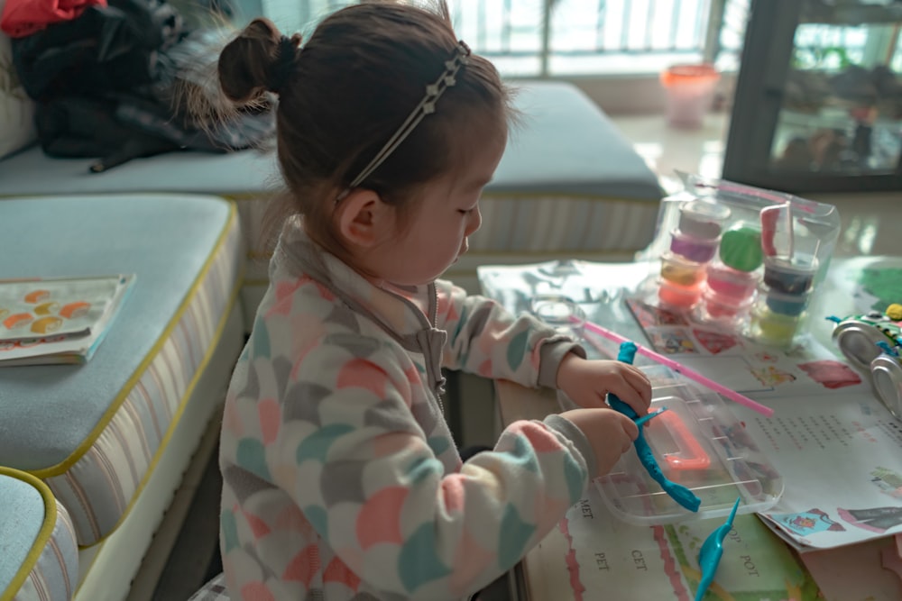 girl in white, teal, and pink jacket playing molding clay