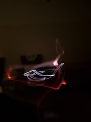 Abstract light painting with swirling patterns of red and white light against a dark background, creating a dynamic and mysterious effect.