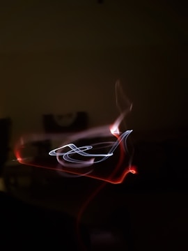 Abstract light painting with swirling patterns of red and white light against a dark background, creating a dynamic and mysterious effect.