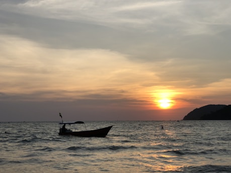 A serene beach scene at sunset with deep blue sea and a small fishing boat.