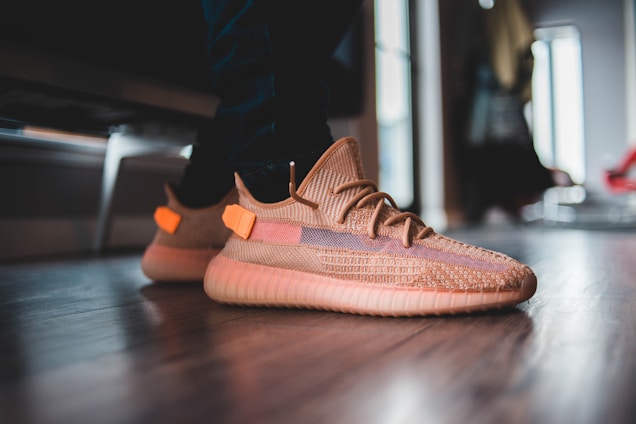 A close-up of stylish, colorful sneakers with a textured design, worn by a person standing on a wooden floor, with a blurred background indicating an indoor setting.