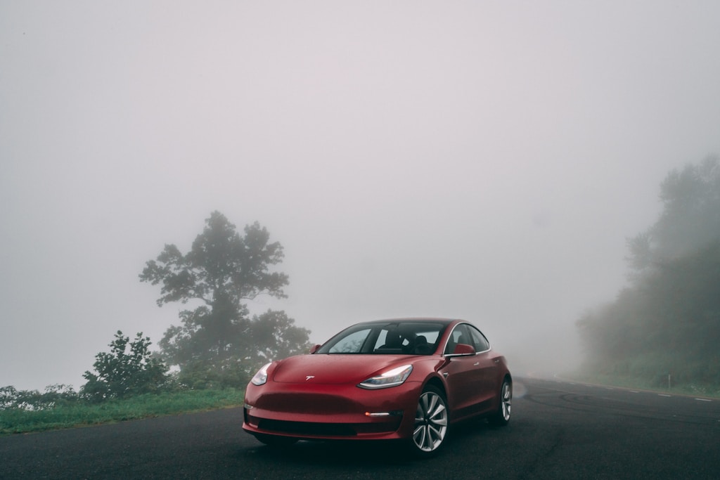 A red self-driving Tesla car on a road during foggy weather.