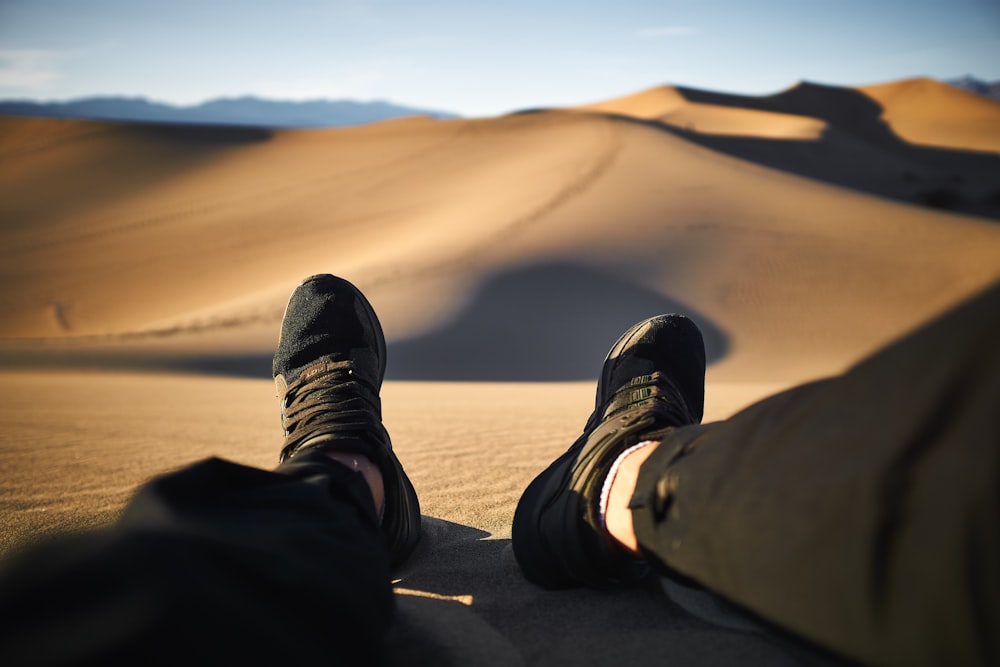 person wearing black pants and pair shoes sitting on desert