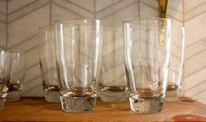 A set of minimalist, clear glass tumblers arranged on a wooden tray with natural light highlighting their smooth curves.