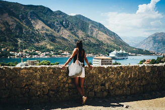 person standing near road looking on sea with different boats on it