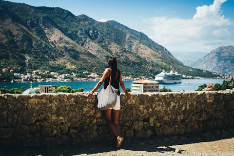 person standing near road looking on sea with different boats on it