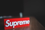 A red rectangular block with the brand name 'Supreme' embossed in white, placed on a wooden surface with a dark blurred background.