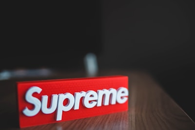 A red rectangular block with the brand name 'Supreme' embossed in white, placed on a wooden surface with a dark blurred background.