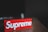 A red rectangular block with the brand name 'Supreme' embossed in white, placed on a wooden surface with a dark blurred background.
