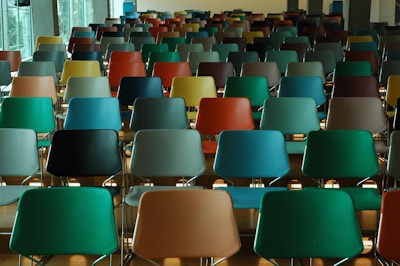 Rows of colorful chairs are neatly arranged in an auditorium or large room with ample natural light coming through large windows. The chairs are empty, creating a sense of anticipation or calm before an event.