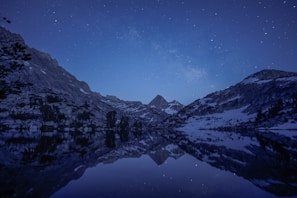 A serene digital landscape of mountains reflected in a calm lake under a starry sky.