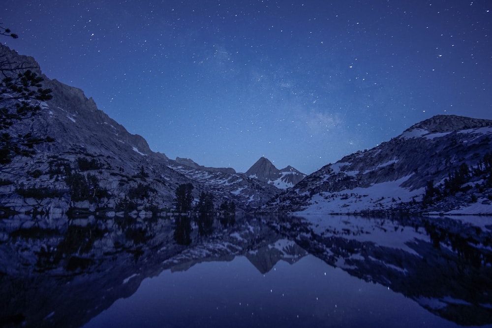 mountain filled with snow near calm body of water during night time